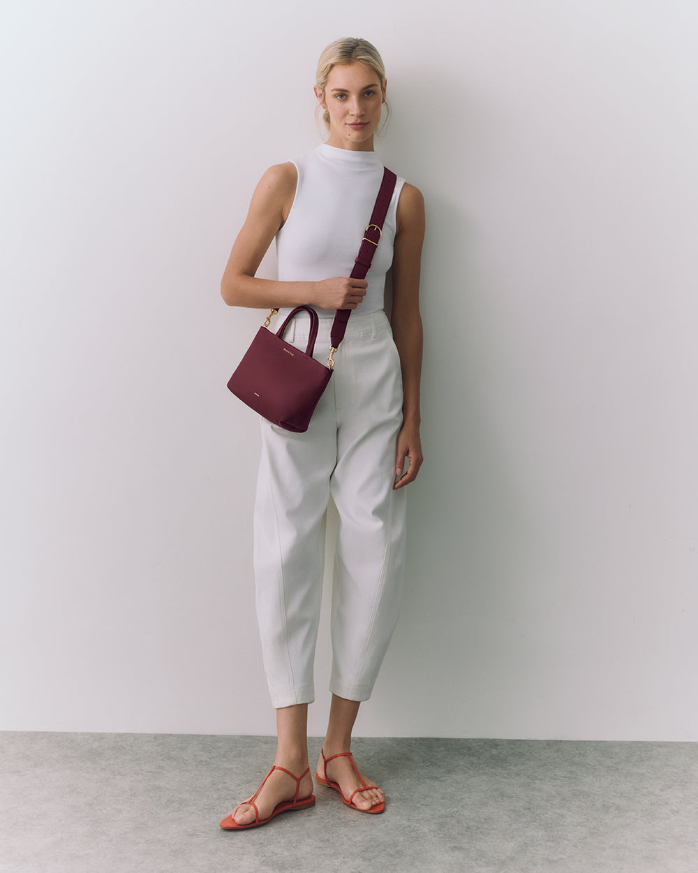 Person poses with a small handbag and is wearing casual attire and sandals.