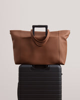 Travel bag with luggage sleeve resting on top of a suitcase with visible handle.