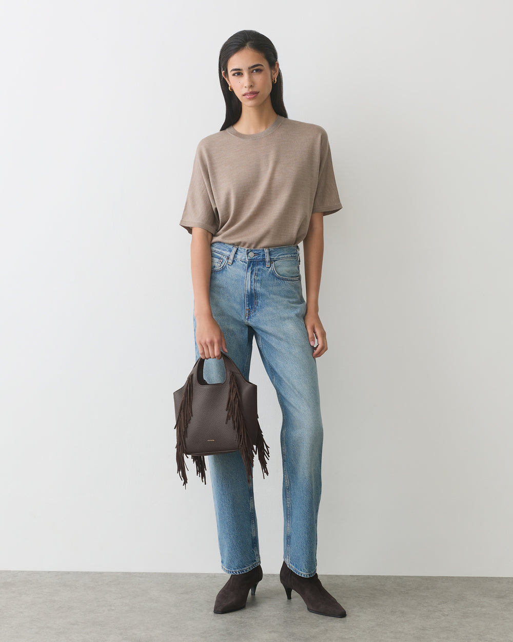 Person in casual outfit holding a fringed handbag, wearing jeans and heels.