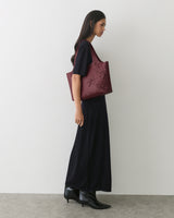 Person in long dress with a floral tote bag and ankle boots standing against a plain background.