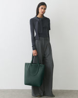 Person wearing sweater and pants holding a large tote bag.