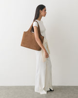 Person in profile holding a large shoulder bag, wearing long pants and a tied shirt.