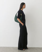 Person standing in profile with handbag on shoulder, wearing wide-leg pants and a short-sleeve top.