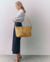 Person in white shirt and long skirt holding a large handbag over shoulder.