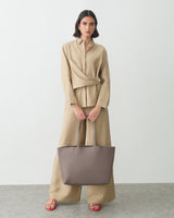 Person in outfit holding a large handbag, standing against plain background.