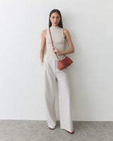 Person in sleeveless top and wide-leg pants holding a shoulder bag.