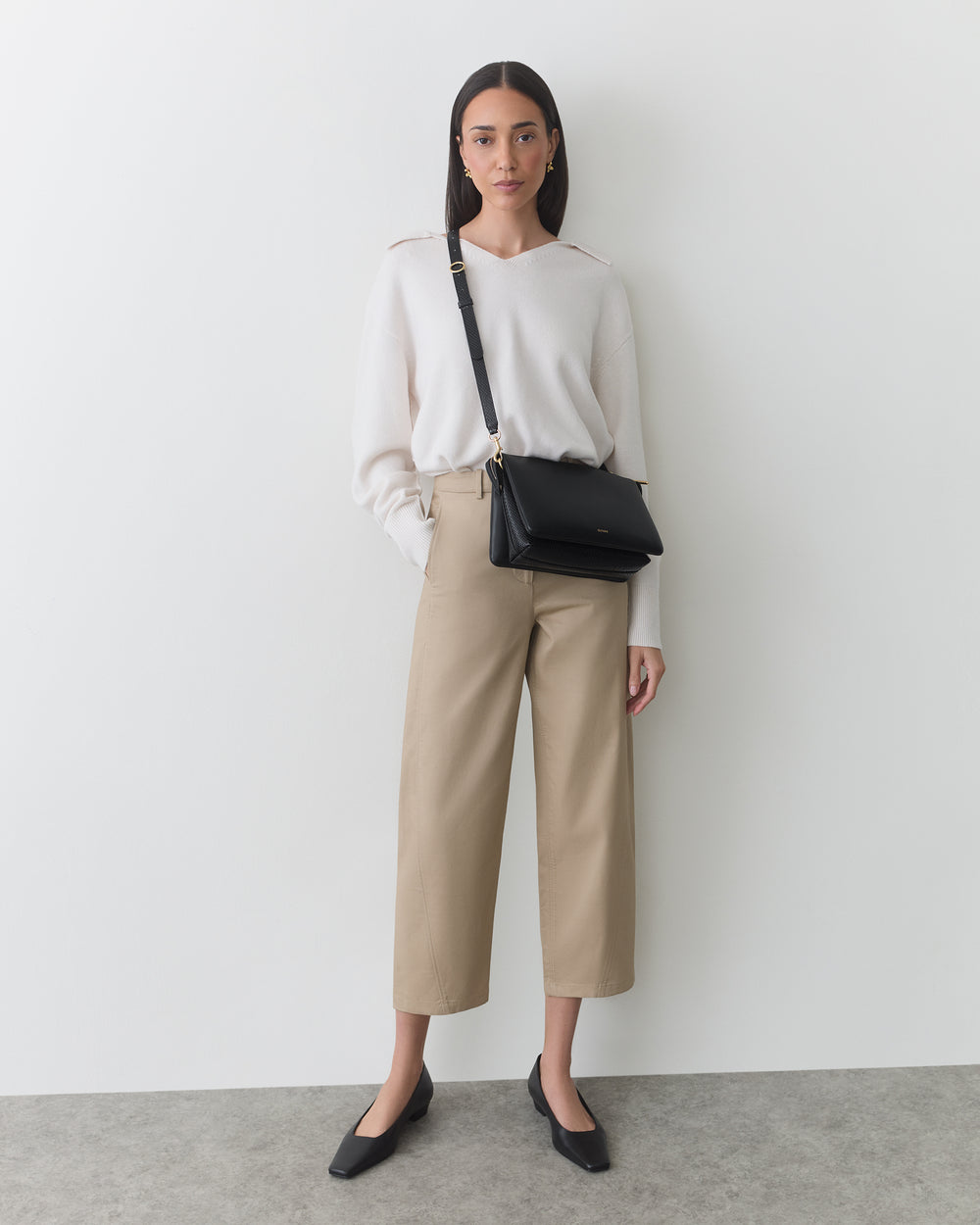 Person standing with a shoulder bag wearing pants and a long-sleeve top.