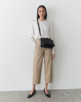 Person standing with a shoulder bag wearing pants and a long-sleeve top.
