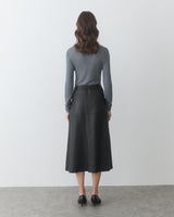 Person facing wall wearing long-sleeve shirt and long skirt.