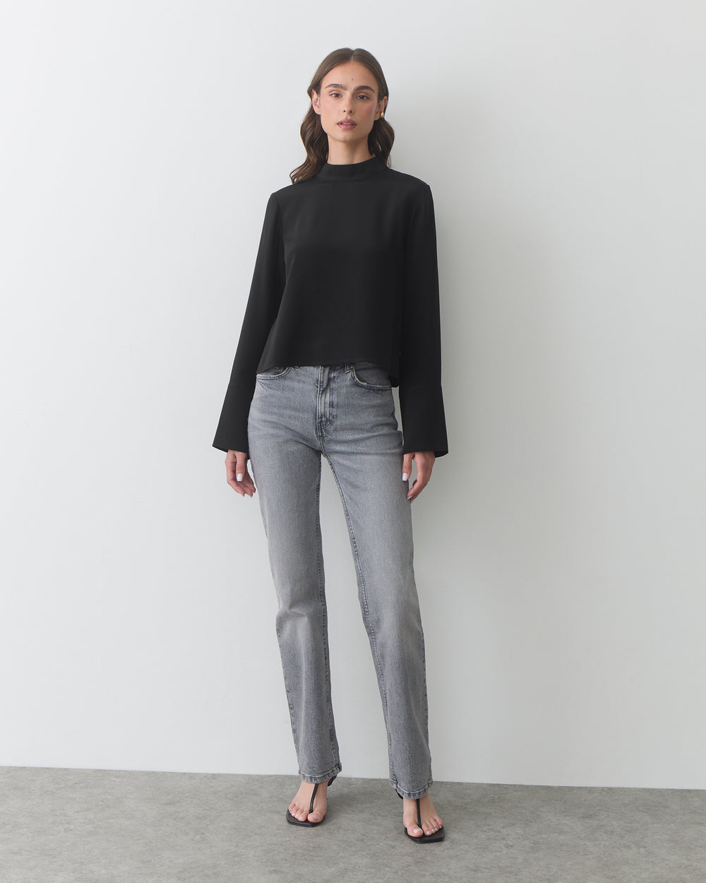 Person in long-sleeve top and jeans, standing on a plain floor.