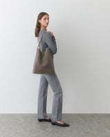 Person carrying shoulder bag, wearing long-sleeve shirt and pants, standing sideways.
