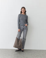 Person standing with a large bag wearing a long-sleeve shirt and jeans.