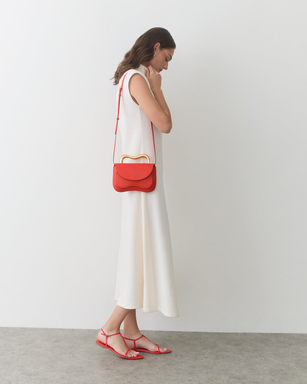Person in sleeveless dress with shoulder bag and sandals stands on concrete floor.