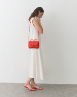 Person in sleeveless dress with shoulder bag and sandals stands on concrete floor.