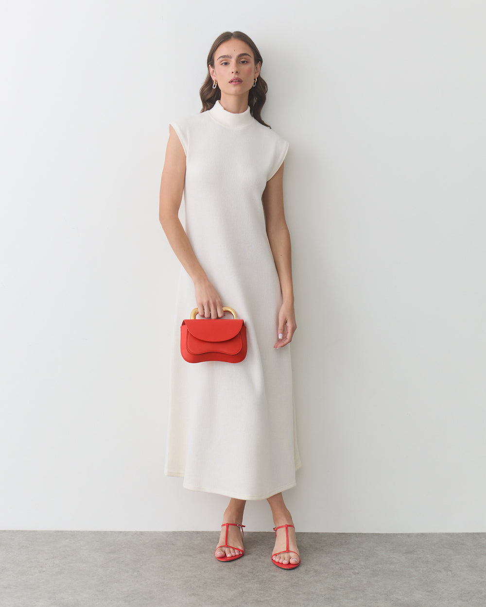 Person in a long dress holding a small handbag, wearing sandals.