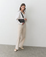 Person in a room holding a purse, wearing a long-sleeve top and wide-leg pants.