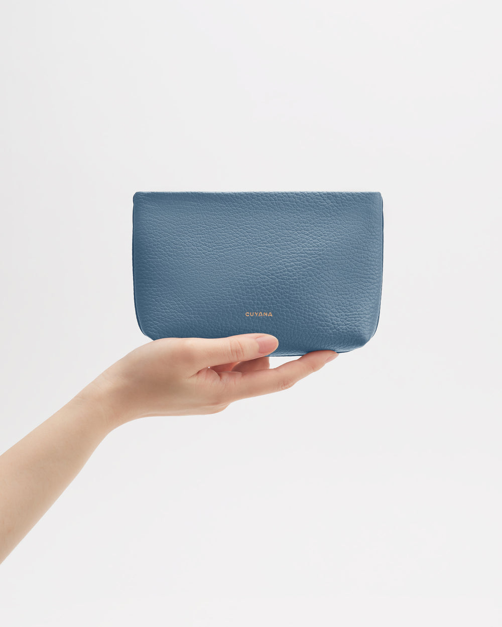 Hand holding a small leather pouch against a plain background.