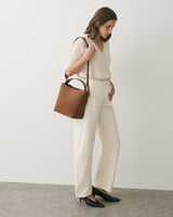 Person wearing v-neck top and pants, holding a shoulder bag, and wearing heeled shoes.
