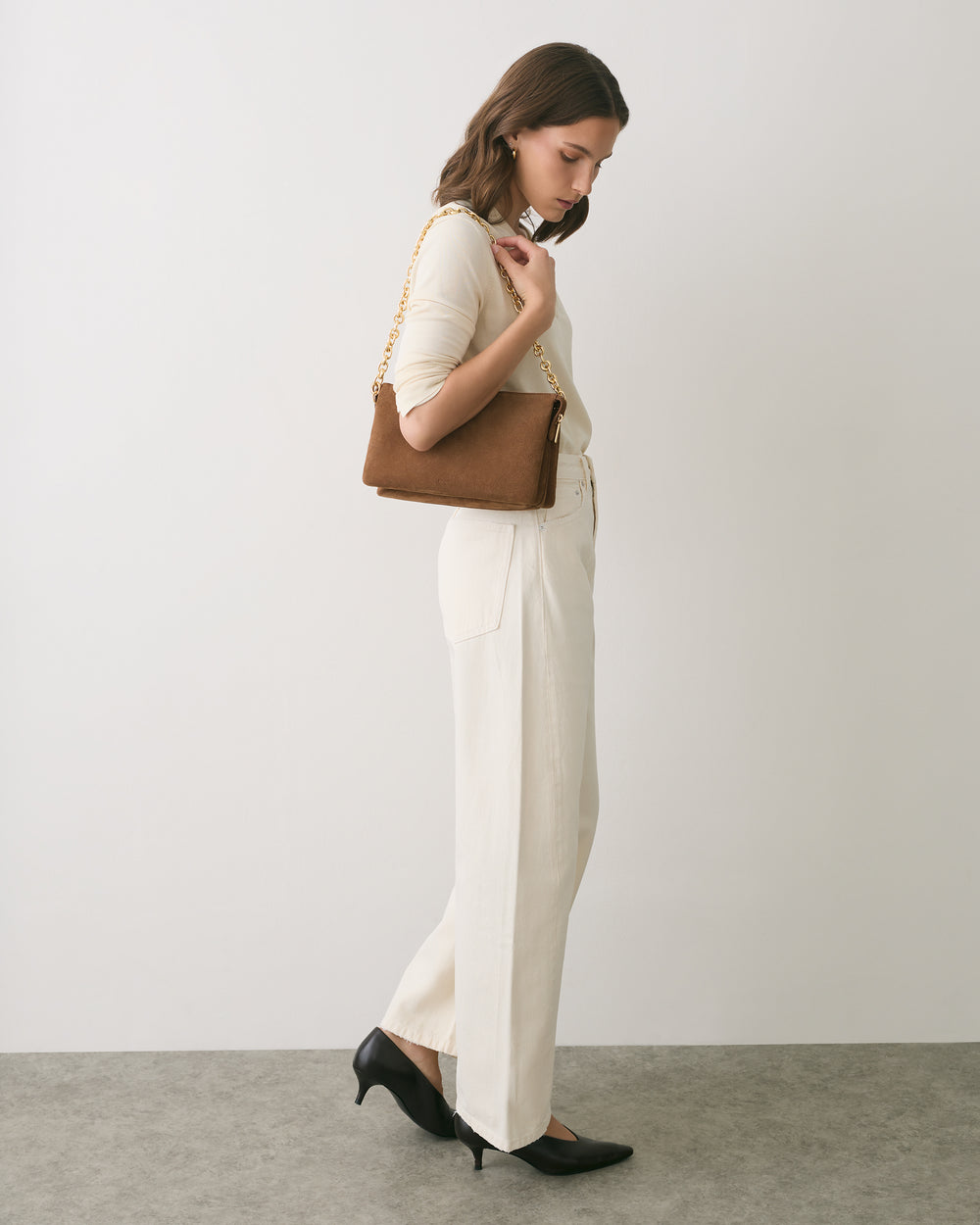 Person standing sideways with a handbag wearing a top and wide-leg pants.