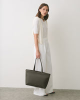 Person standing, holding a handbag, wearing a light top and pants.