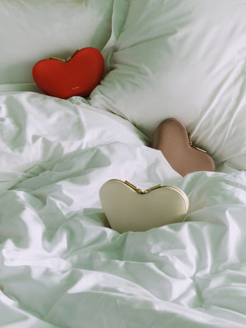 Three heart-shaped purses on a bed with pillows.