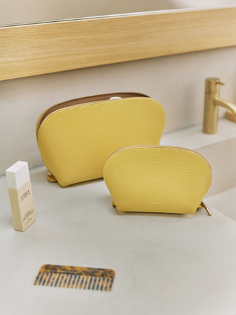 Two cosmetic bags on a bathroom counter with a comb and a bottle nearby.