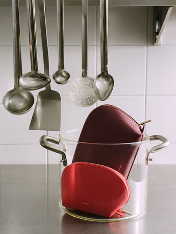Two pouches in a glass pot beneath hanging kitchen utensils.
