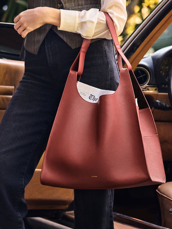 Person holding a large handbag with a newspaper inside near a car door.