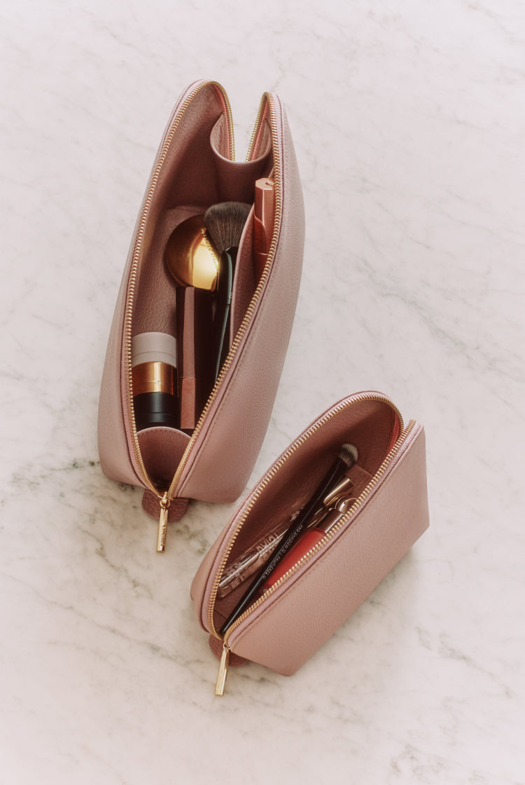 Two makeup bags with cosmetics and brushes inside on a marble surface.