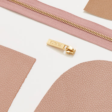 Zipper with slider and fabric pieces arranged on a surface.