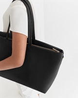 Person carrying a large handbag with zip detail.