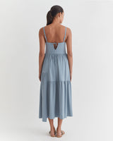Woman seen from behind, wearing a mid-length dress, standing indoors.
