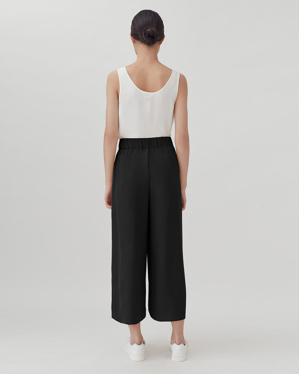 Woman in a sleeveless top and cropped pants standing facing away.