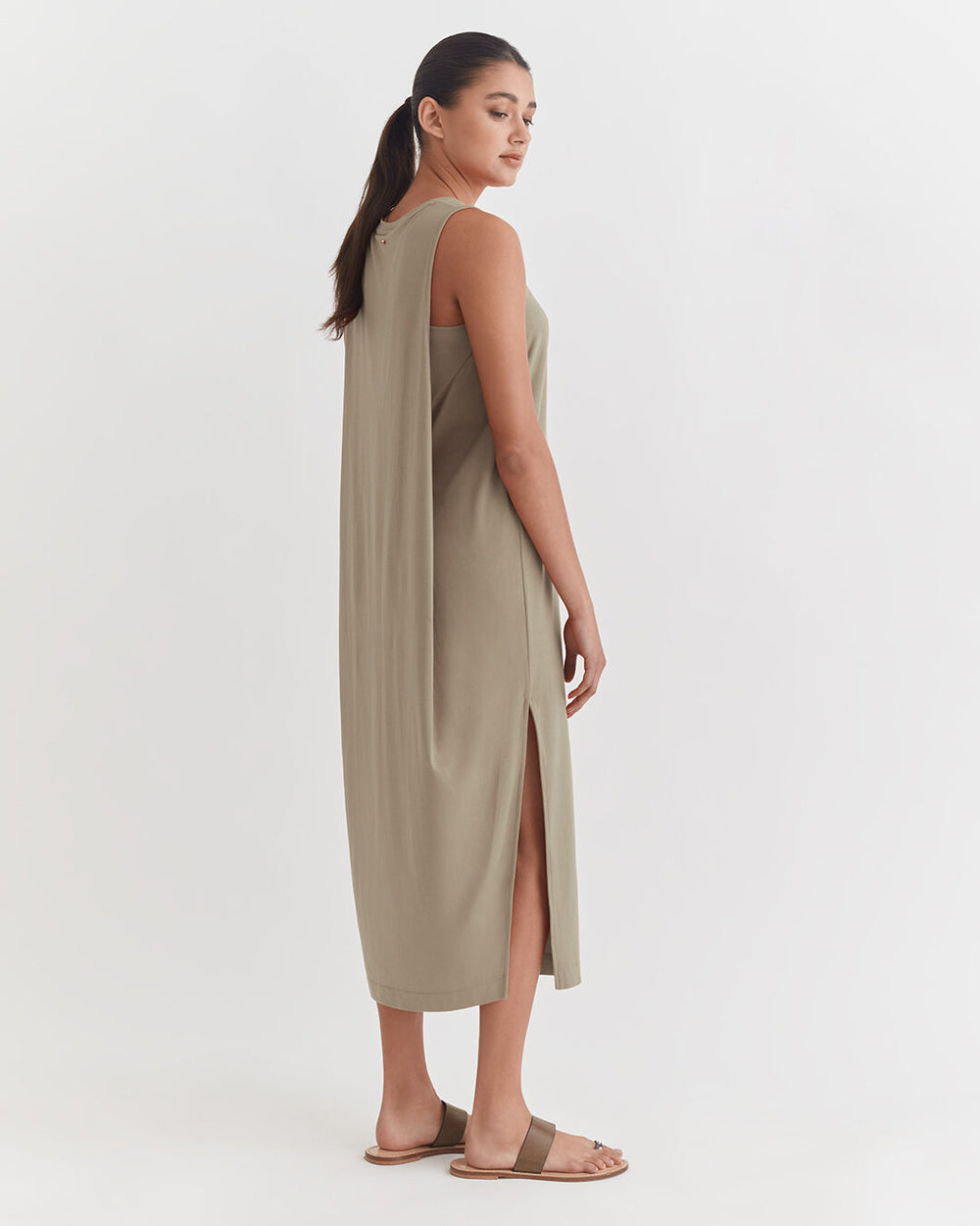 Woman in a sleeveless long dress standing sideways, looking over shoulder.