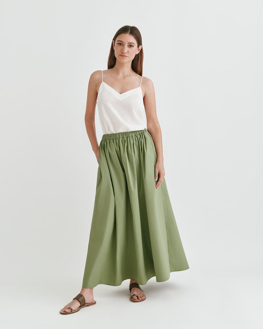 Woman in a sleeveless top and long skirt standing in a studio.