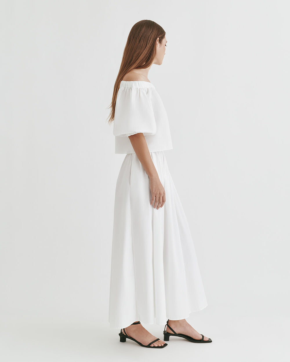 Woman standing sideways in a short-sleeved top and long skirt.