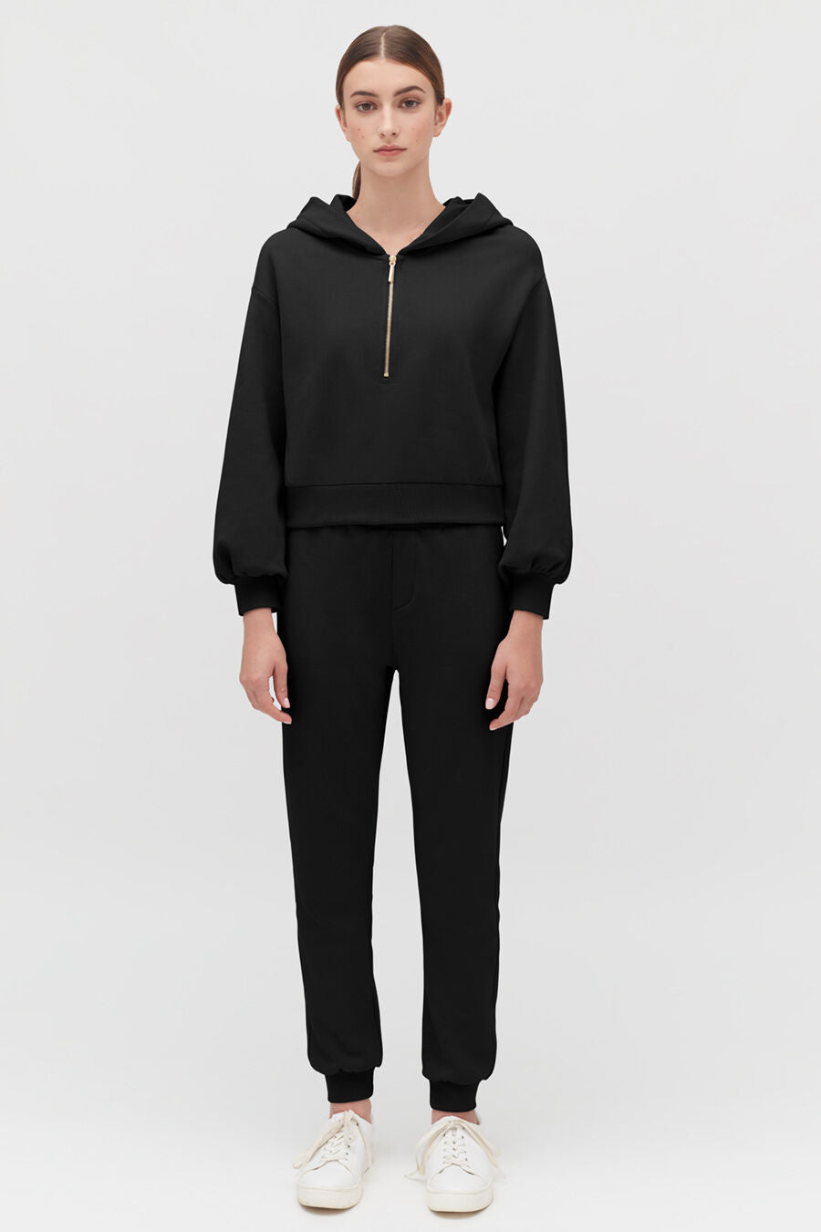 Woman standing in hoodie and pants with sneakers.