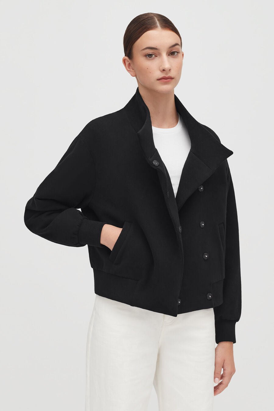 Woman in a jacket and pants standing with hands in pockets.