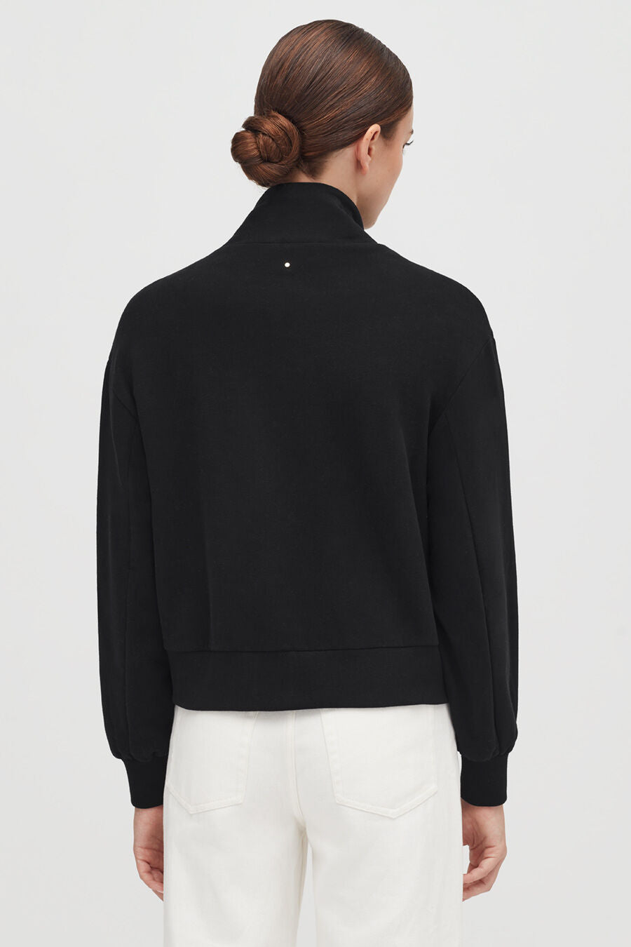 Woman seen from the back with hair in a bun, wearing a jacket and pants.