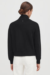 Woman seen from the back with hair in a bun, wearing a jacket and pants.