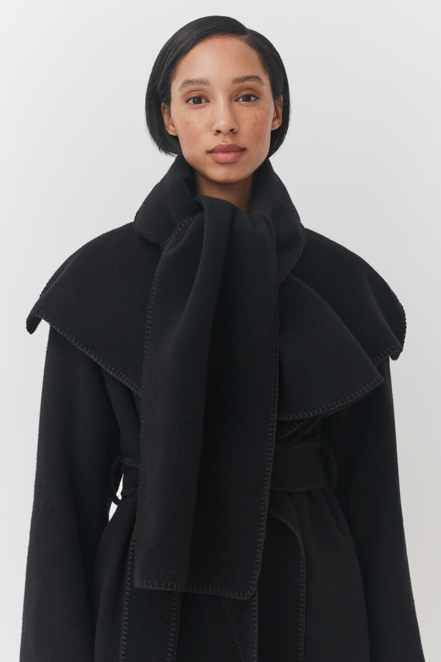 Woman wearing a belted coat with a high collar.
