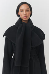 Woman wearing a belted coat with a high collar.