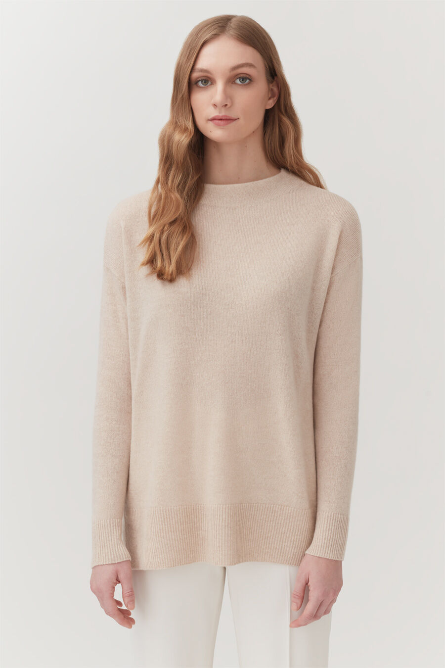 Woman standing in a sweater and pants, looking at the camera.