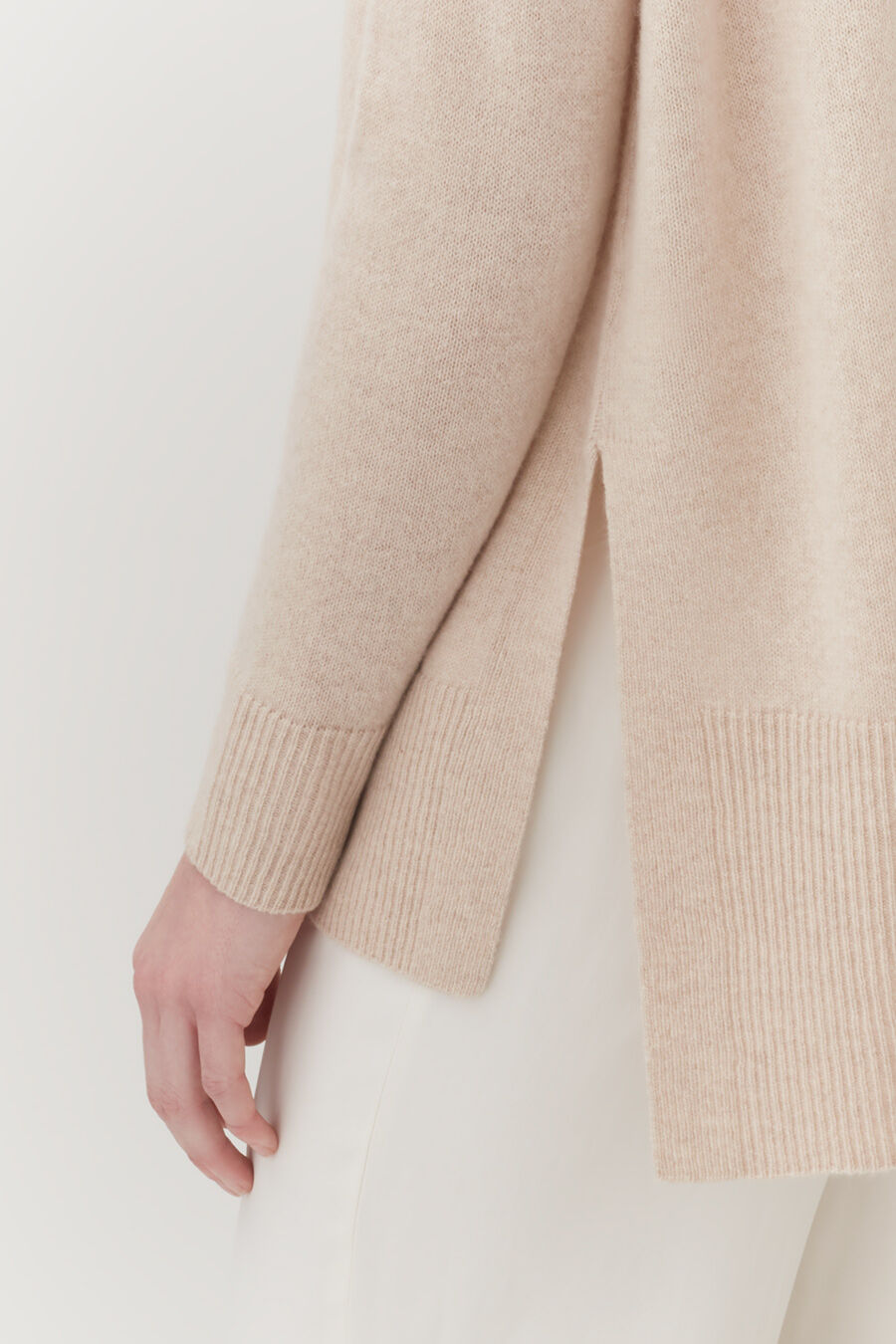 Close-up of a person's hand beside a sweater sleeve and skirt edge.