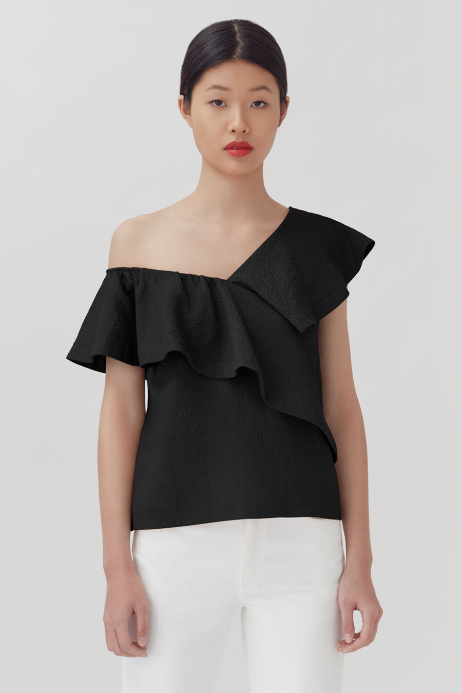 Woman in an off-shoulder top with ruffle detail, standing against a plain background.