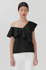 Woman in an off-shoulder top with ruffle detail, standing against a plain background.