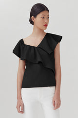 Woman standing in a one-shoulder ruffled top and pants looking to the side.