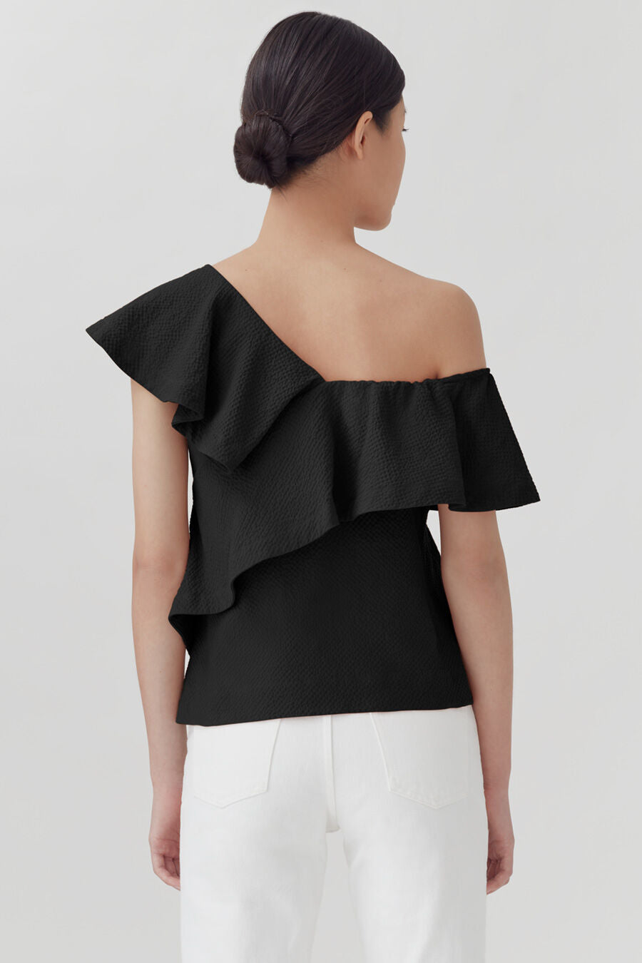 Woman from behind with a ruffled off-shoulder top and hair in a bun.