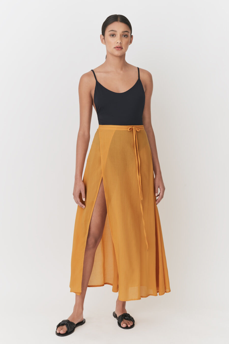 Woman in tank top and long skirt with split, standing straight.