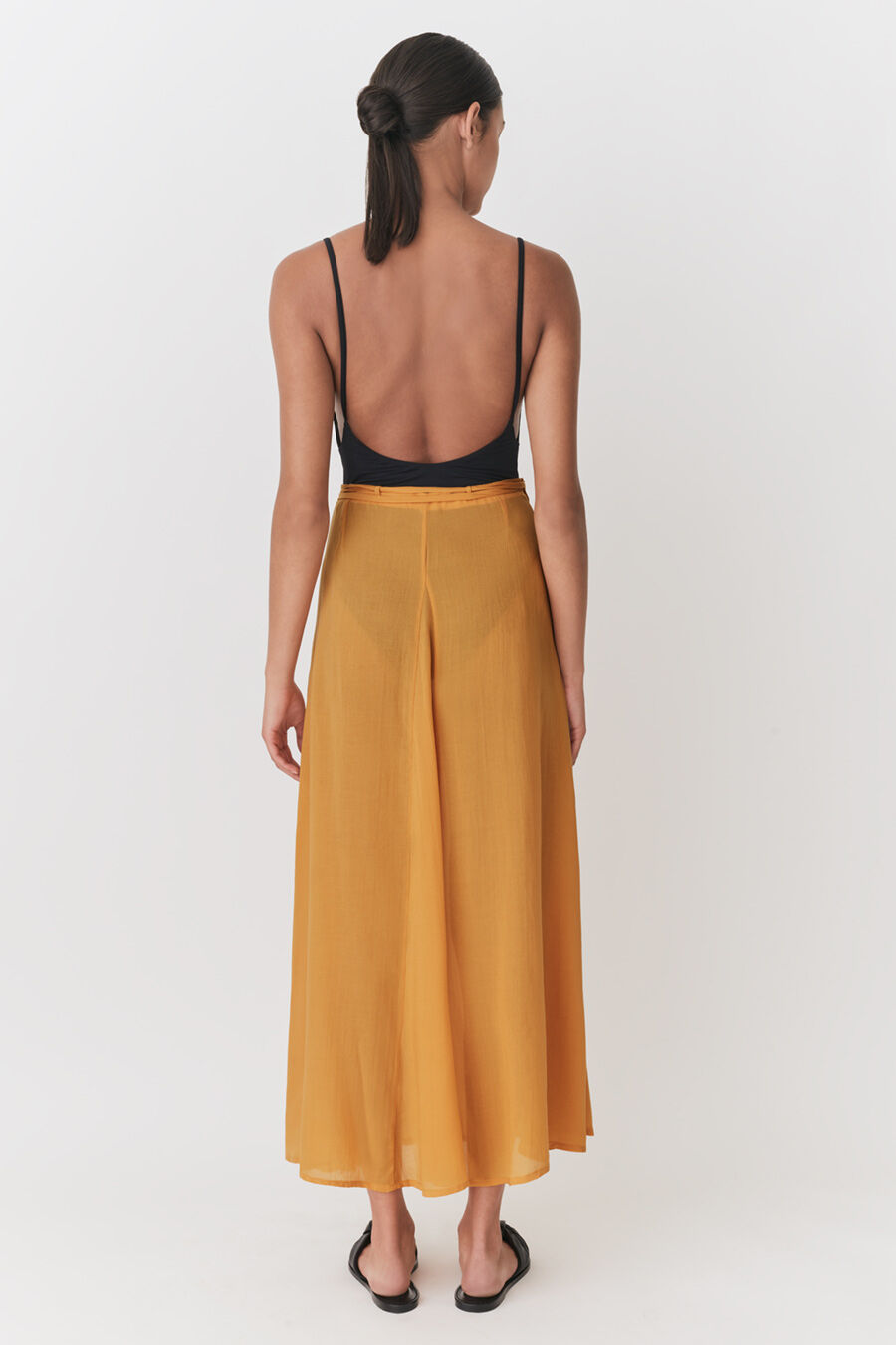 Woman viewed from behind wearing a tank top and long skirt, standing upright.